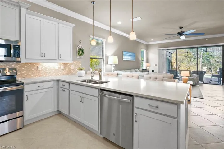 Kitchen featuring stainless steel appliances, decorative backsplash, ornamental molding, light stone countertops, and hanging light fixtures