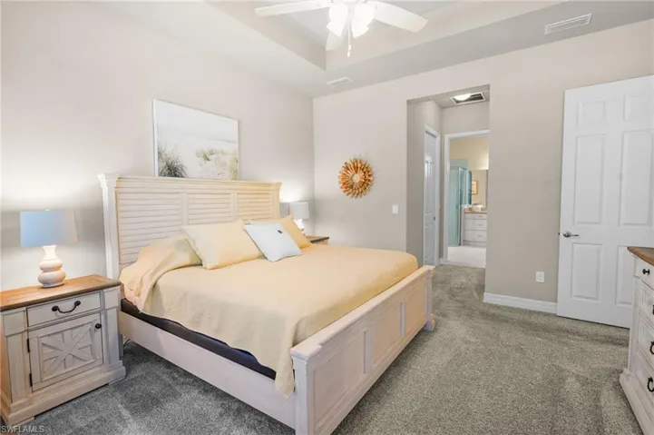 Bedroom with light colored carpet, a raised ceiling, connected bathroom, and a ceiling fan