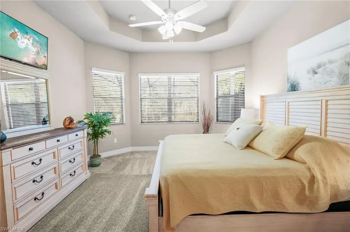 Bedroom with a ceiling fan, a tray ceiling, and light colored carpet