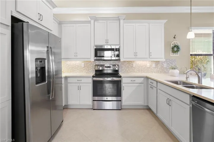 Kitchen with stainless steel appliances, white cabinetry, light stone countertops, backsplash, and ornamental molding