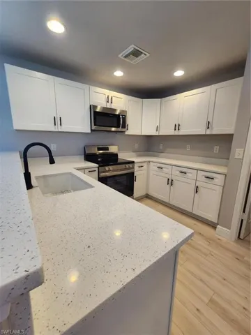 Kitchen with stainless steel range, light hardwood / wood-style flooring, sink, and white cabinetry