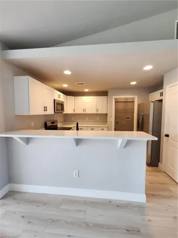 Kitchen with stove, white cabinets, light wood-type flooring, fridge, and kitchen peninsula