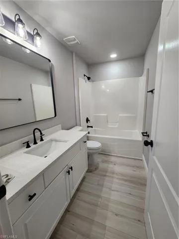 Full bathroom featuring washtub / shower combination, toilet, vanity, and hardwood / wood-style flooring