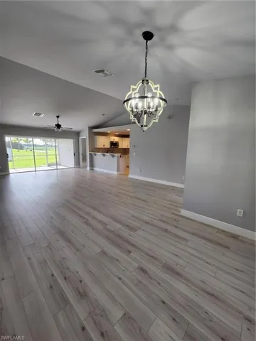 Unfurnished living room with light wood-type flooring, ceiling fan with notable chandelier, and vaulted ceiling