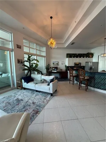 Living area featuring crown molding, a raised ceiling, light tile patterned floors, and a chandelier