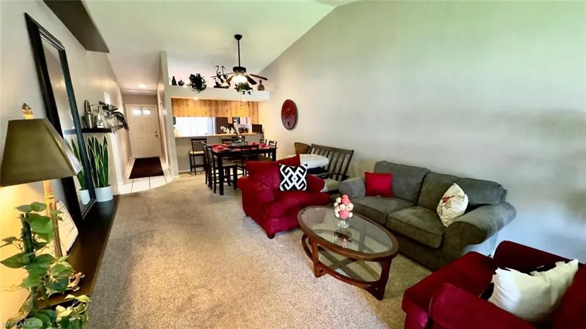 Living area featuring vaulted ceilings, a ceiling fan with light fixture, and carpet flooring