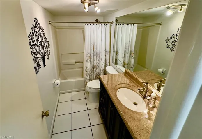 Guest Bathroom featuring a built-in tub with shower, white tile flooring, a single vanity with an oval sink, a light-toned countertop, and a large wall-mounted mirror