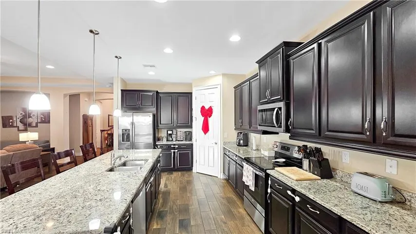 Kitchen with light stone countertops, appliances with stainless steel finishes, dark wood-type flooring, sink, and hanging light fixtures