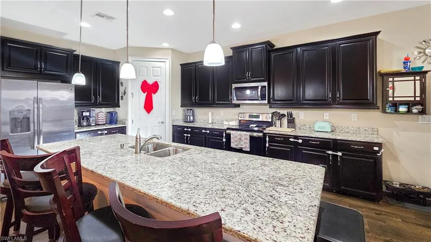 Kitchen featuring dark wood-type flooring, sink, an island with sink, appliances with stainless steel finishes, and decorative light fixtures