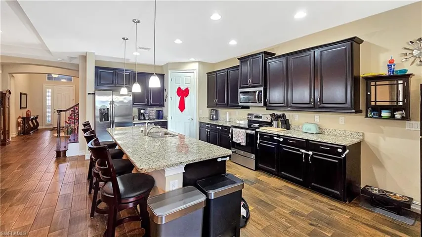 Kitchen with a center island with sink, pendant lighting, stainless steel appliances, and dark wood-type flooring