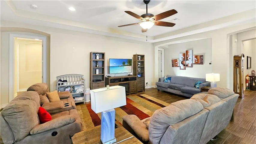 Living room with a raised ceiling, ceiling fan, and dark hardwood / wood-style floors