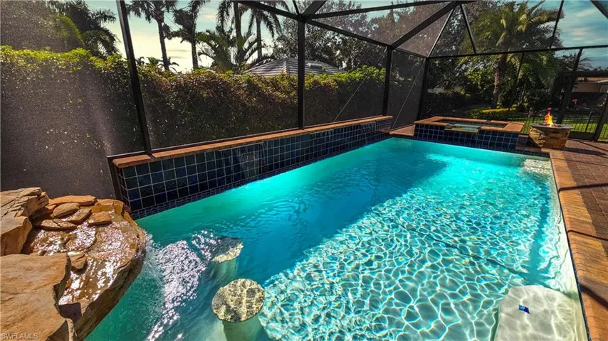 Pool at dusk featuring glass enclosure and an in ground hot tub