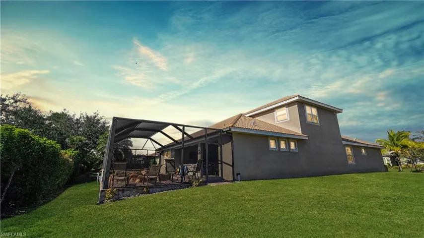 Back house at dusk featuring a patio, a lanai, and a lawn