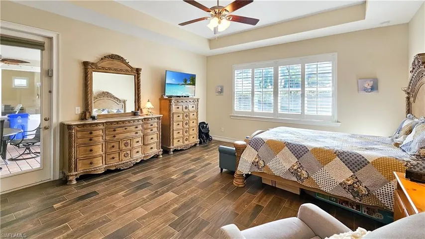 Bedroom featuring access to exterior, dark hardwood / wood-style floors, ceiling fan, and a tray ceiling
