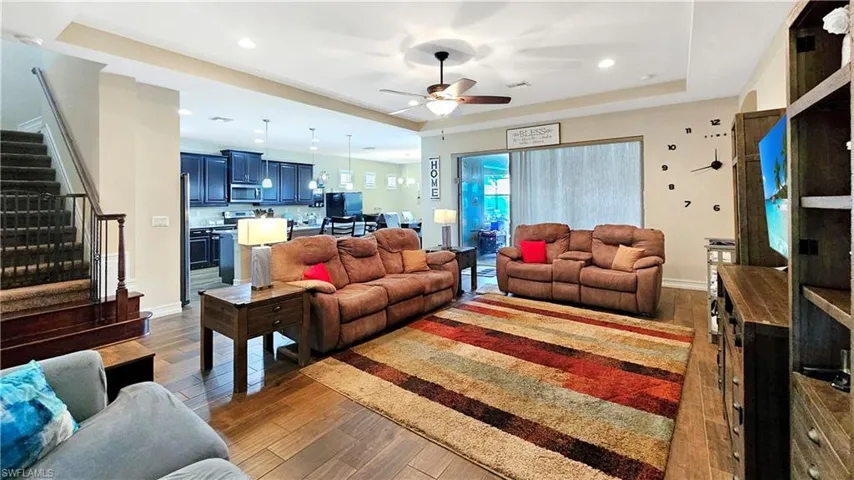 Living room with dark hardwood / wood-style floors, ceiling fan, and a tray ceiling