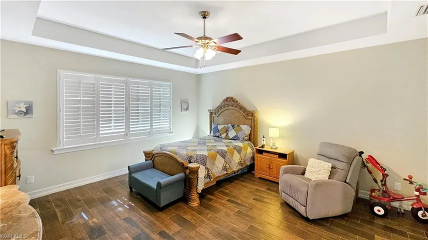 Bedroom with a raised ceiling, ceiling fan, and dark wood-type flooring