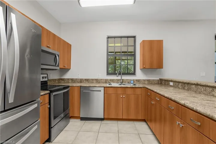 Kitchen with stainless steel appliances, wood finish cabinetry, light tile patterned floors, and light stone countertops