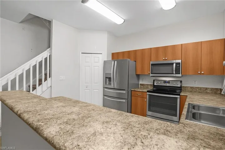 Kitchen with stainless steel appliances, wood finish cabinets, a peninsula, and light stone counters