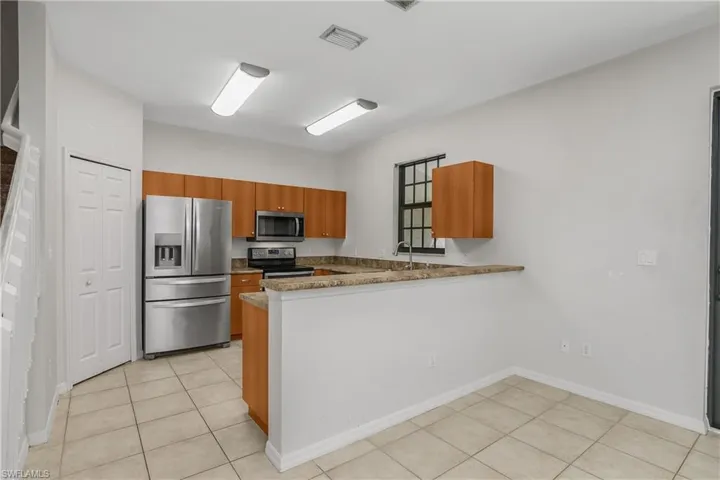 Kitchen featuring stainless steel appliances, wood finish cabinets, a peninsula, light tile patterned floors, and dark stone counters