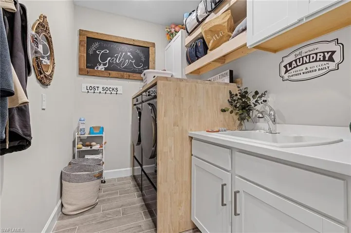 Clothes washing area featuring sink, washing machine and clothes dryer, cabinets, and light hardwood / wood-style floors