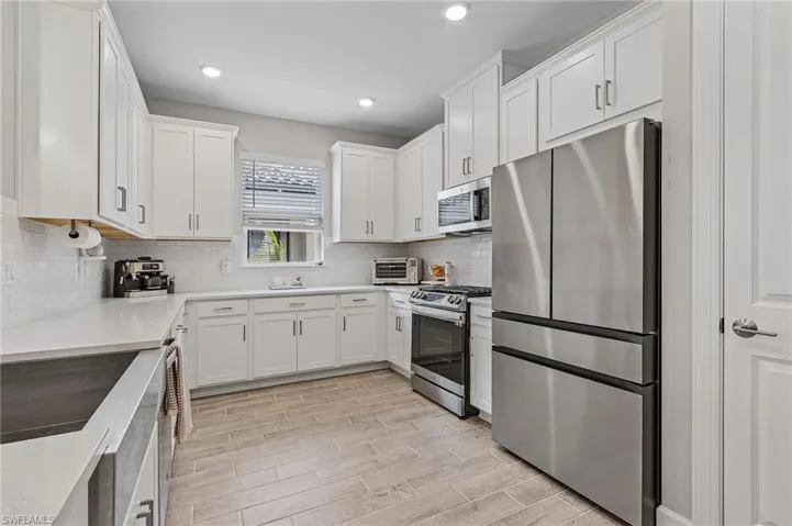 Kitchen with backsplash, stainless steel appliances, white cabinetry, and light hardwood / wood-style flooring