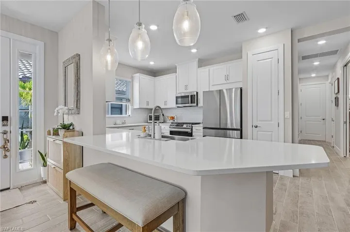 Kitchen with light hardwood / wood-style flooring, decorative backsplash, white cabinetry, stainless steel appliances, and pendant lighting
