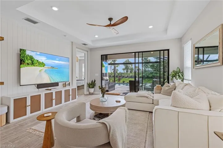 Living room with ceiling fan, a raised ceiling, and light hardwood / wood-style floors