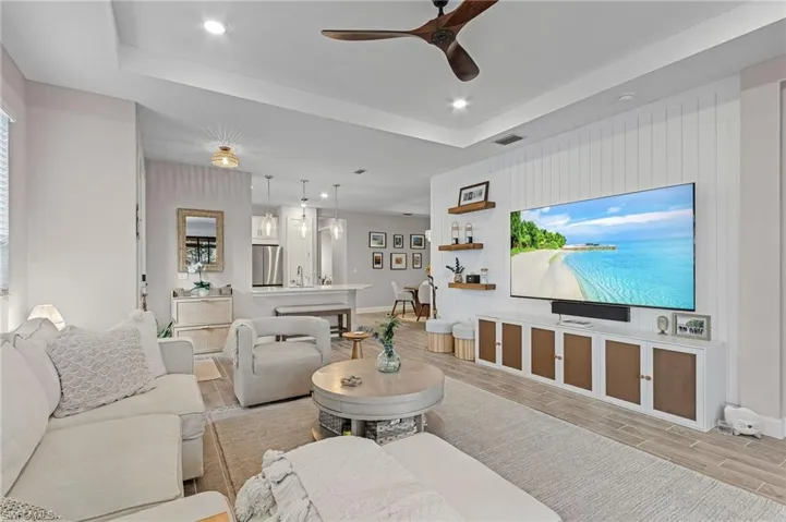 Living room with ceiling fan, a raised ceiling, and light wood-type flooring