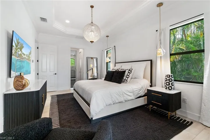 Bedroom with multiple windows, ornamental molding, light wood finished floors, and a raised ceiling