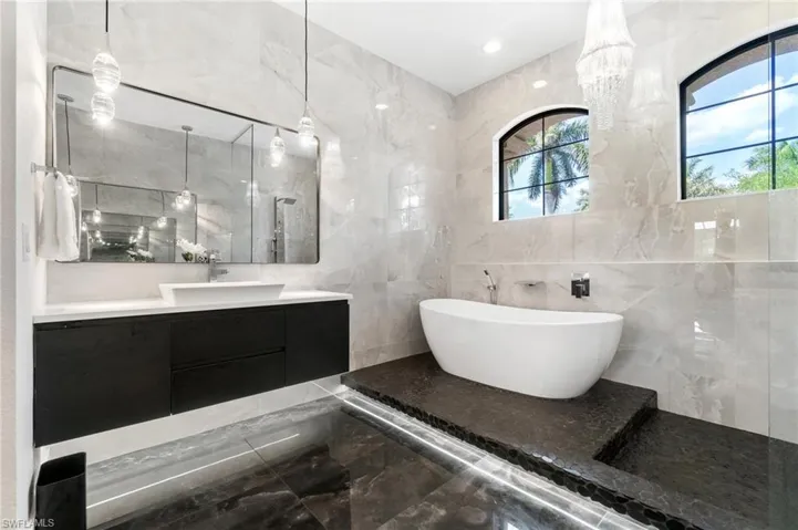 Bathroom with marble tiled floors, a freestanding bath, tile walls, vanity, and walk in shower