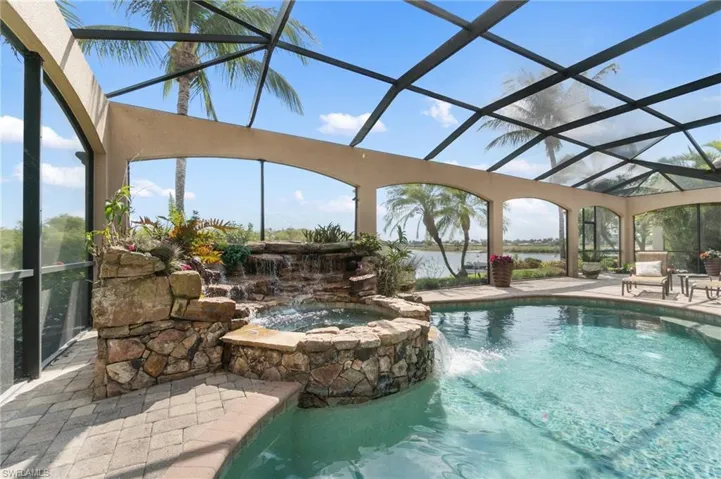 View of swimming pool featuring glass enclosure, a patio, a pool with connected hot tub, and a water view