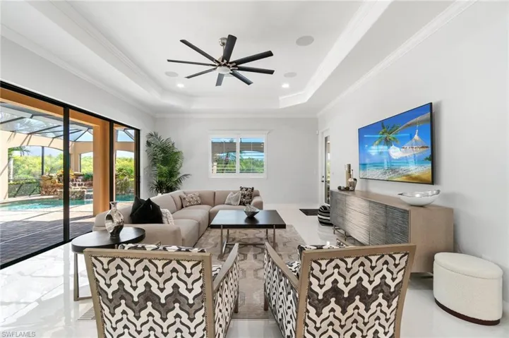 Living area with a raised ceiling, ceiling fan, and ornamental molding