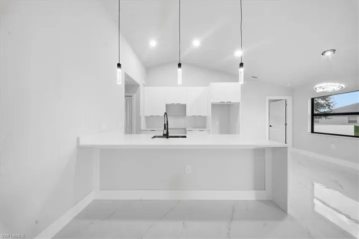 Kitchen featuring a peninsula, light stone counters, white cabinets, lofted ceiling, and hanging light fixtures