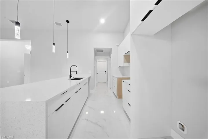 Kitchen with white cabinets, a peninsula, hanging light fixtures, light marble finish floors, and modern cabinets