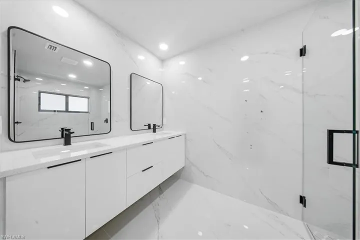 Bathroom with light marble finish floors, double vanity, stone wall, a marble finish shower, and recessed lighting