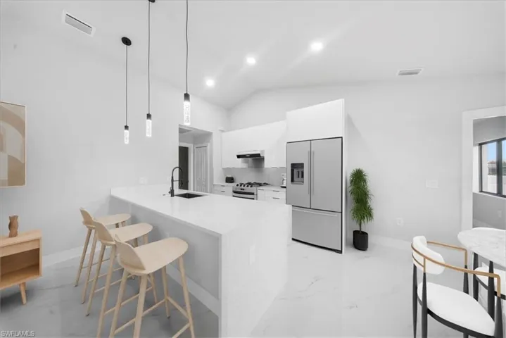 Kitchen with high quality fridge, a peninsula, decorative light fixtures, a breakfast bar area, and white cabinets