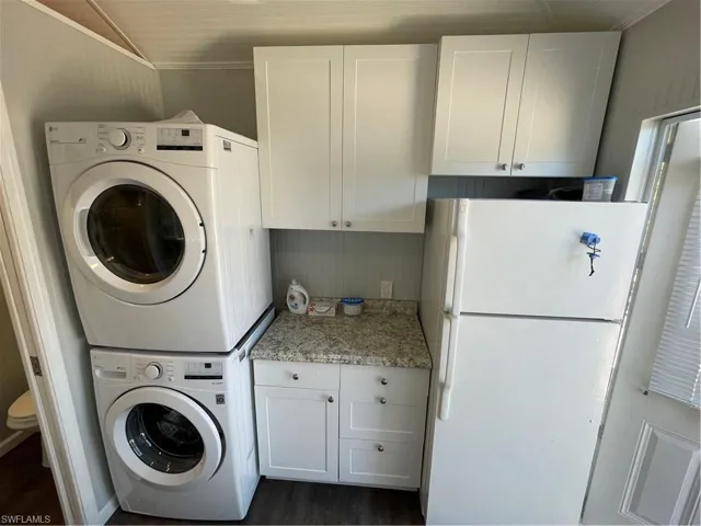 Laundry room featuring stacked washer / drying machine, dark hardwood / wood-style flooring, cabinets, and ornamental molding