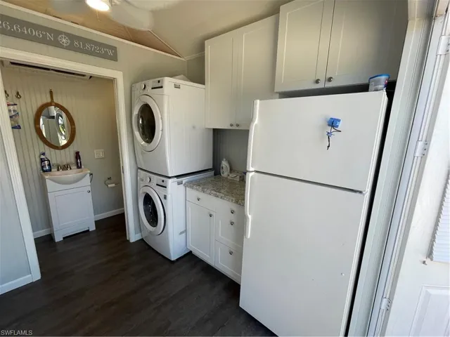 Clothes washing area featuring cabinets, stacked washer / drying machine, sink, and dark wood-type flooring