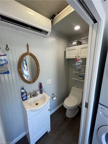 Bathroom featuring a wall mounted air conditioner, vanity, stacked washer and clothes dryer, hardwood / wood-style flooring, and toilet