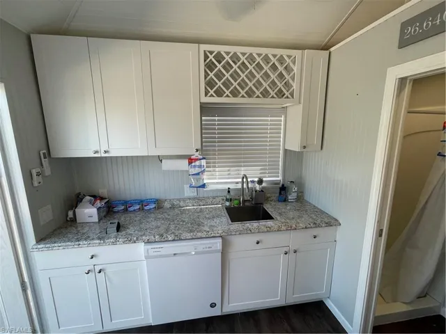 Kitchen featuring dishwasher, sink, light stone counters, dark hardwood / wood-style flooring, and white cabinets