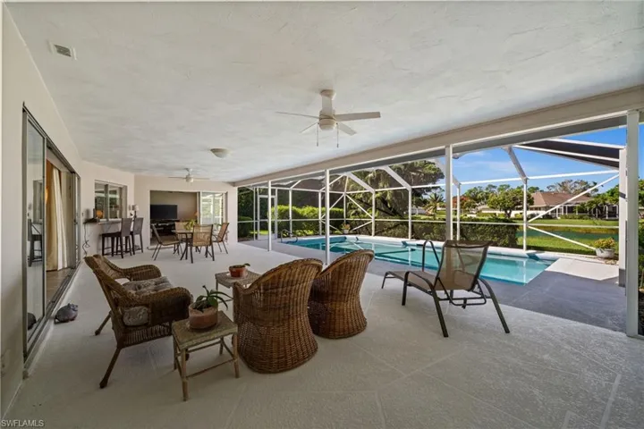 The expansive covered lanai offers inviting spaces for lounging and outdoor dining, overlooking the screened pool and peaceful lake beyond.
