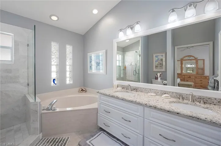 Primary Bathroom featuring tile patterned floors, 2 sing vanity with drawers, separate shower and tub, and lofted ceiling