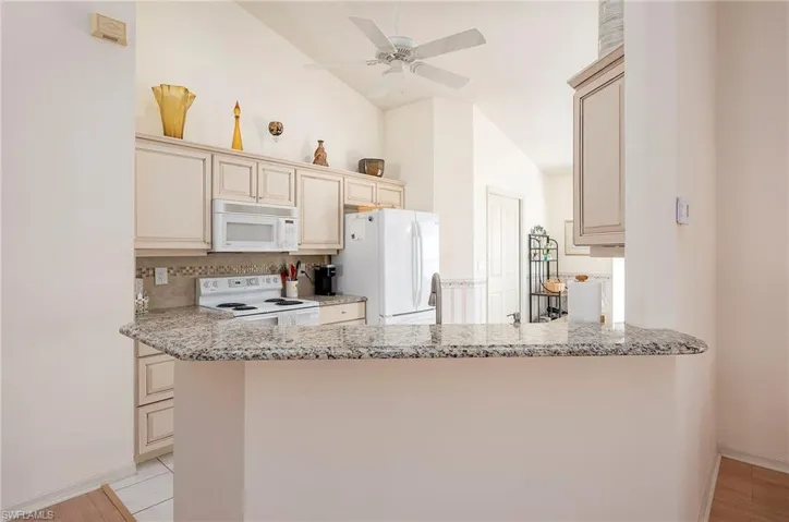 Kitchen with vaulted ceiling, white appliances, and cream cabinetry