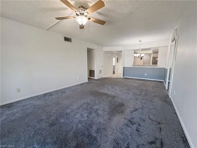 Unfurnished living room with dark colored carpet, a ceiling fan, a chandelier, and a textured ceiling