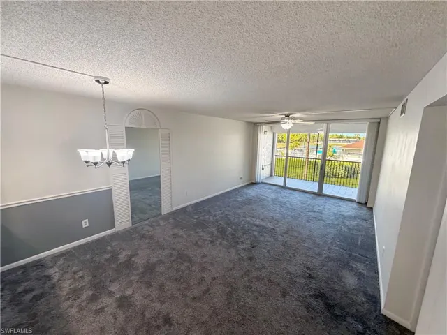 Empty room featuring floor to ceiling windows, a ceiling fan, dark carpet, a textured ceiling, and suspended lighting