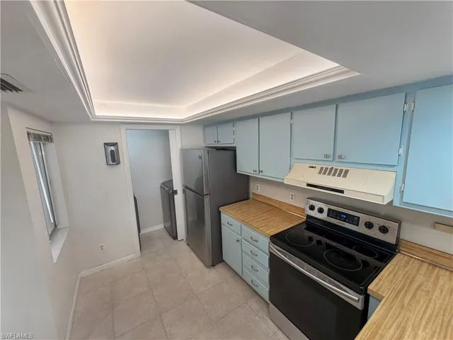 Kitchen featuring stainless steel appliances, light countertops, ventilation hood, a tray ceiling, and blue cabinets