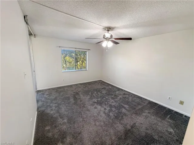 Empty room with dark colored carpet, a textured ceiling, and ceiling fan