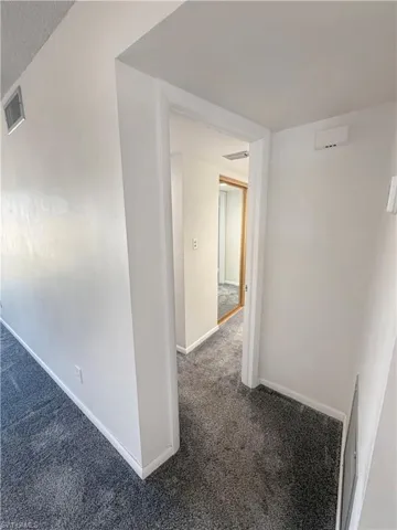 Hallway featuring dark colored carpet and baseboards
