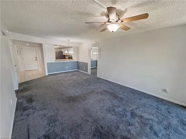 Unfurnished living room featuring ceiling fan, dark colored carpet, and a textured ceiling