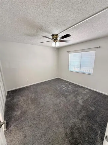 Empty room with dark colored carpet, a textured ceiling, and a ceiling fan